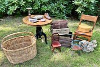 Full lot including industrial crank table with distressed round wood top, assorted vintage collectibles and chairs arranged on grass.