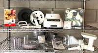 Overview photo showing all items including the food processor base, attachments, discs, bowls, manual, cookbook, and sausage stuffer on wire shelving