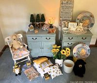 Wide view of Pooh Corner collection with stuffed bear, two blue chests, plates, towels, and various decor items arranged on floor and furniture.