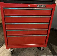 Front view of red Husky tool cabinet with all five drawers closed and caster wheels visible.