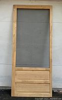 Full view of the unfinished wooden screen door showing the wooden frame, lower solid panels, and top screen section.