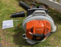 Main unit on grass with one blower tube, instruction manual, T-wrench and screwdriver laid out