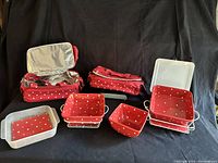 Image of two red polka dot insulated casserole carriers, three matching deep polka dot dishes (one with cover), and two vinyl trivets with dotted glass inserts