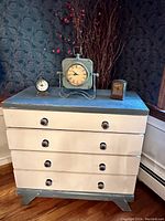 Front view of pine dresser with three clocks on top against patterned wallpaper background.