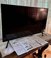 Full front view of the Toshiba Fire TV Edition 43 inch Smart TV on a wooden table with instruction pamphlet and remote control in front of it.