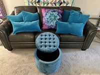 Full view of six arctic blue synthetic suede throw pillows (4 square 20x20, 2 rectangular 18x11), one floral square center pillow, and matching tufted round ottoman stool on a sofa.