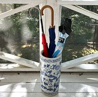 Umbrella stand holding three umbrellas, showing chrome, wooden, and plastic/rubber handles.