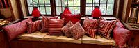 Window seat with eight red throw pillows arranged along the back cushion and three red glass candle lanterns placed on the windowsill behind them