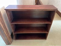 Front view of the bookshelf showing three fixed shelves inside a birch veneered frame in medium brown finish.