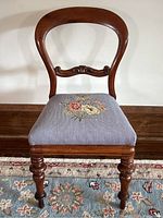 Front view of antique balloon back chair showing balloon shaped wooden back and floral embroidered blue seat cushion.