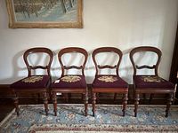 Four antique balloon back chairs arranged side-by-side showing ornate backs and embroidered seats.