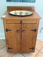 Full view of the antique pine washstand showing cupboard with two doors, wooden knobs, and black iron hinges and latch, topped by a hand-painted ceramic basin.