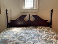 Front view of antique style solid wood queen headboard with mahogany stain, showing carved central finial and shaped top, attached to mattress for scale.