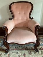 Front view of Victorian gentleman’s chair showing pink velvet upholstery and carved wood frame with button tufting on backrest