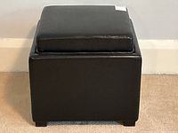 Front view of black leather square ottoman showing the cushioned removable top and base.