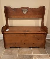 Front view of carved pine blanket box bench with heart cutout on backrest and scalloped base edge.
