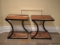 Front view of two matching industrial style end tables showing the wood shelves and curved black metal frame.