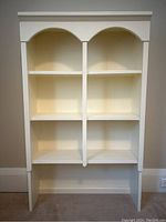 Front view of white painted pine shelf with arched top showing three shelves on each side and two vertical supports dividing into six compartments.
