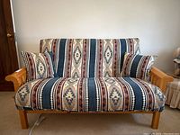 Front view of pine wood frame futon with patterned cushions and two pillows.