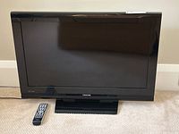 Full front view of Toshiba flat screen TV on stand with remote control placed in front on carpet.