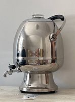 Full view of the chrome samovar showing reflective polished surface, black handle, and chrome base.