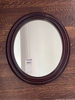 Clear overhead photo of the oval mirror on wood floor showing full frame and glass.