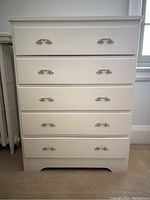 Front view of white painted vintage solid wood highboy dresser with five drawers, ornate metal handles, and base cutout detail.