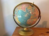 Front view of vintage world globe on gold metal stand showing continents and oceans