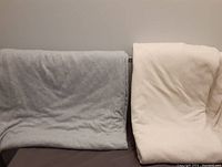 Two folded sheets, one light gray and one neutral cream color, placed on a flat surface to show color and texture.