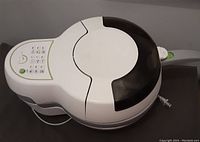 Electric air fryer showing full unit with digital control panel on top, white and gray plastic body with black lid, power cord visible.