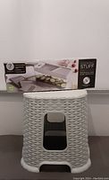 Photo showing gray plastic rattan stepping stool with woven texture and opening handles