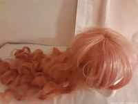 Photo shows the pink synthetic wig with curls and bangs, long length