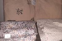 Photo shows a folded set of neutral beige linens including a floral printed sheet and two plain fabric pieces, some with tags attached.