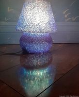 Retro royal blue jelly mushroom table lamp illuminated on a hardwood floor showing its textured glass surface and light diffusion effect.
