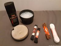 Overall display of shoe polish items including black liquid polish, dubbin grease tub, two applicator pads, and five sets of shoe laces