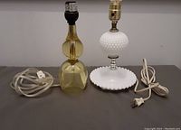 Two vintage table lamps side by side showing yellow resin one and white hobnail glass one with cords and lamp sockets visible.
