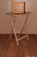 Image shows vintage wood swivel organizer placed on top of new wood folding table, both standing on wooden floor against neutral wall.