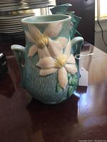 Front view showing floral Clematis design on blue-green vase background with two side handles.