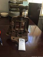 Front angle view of the vintage cast iron vise on a wooden table next to a pen for scale, showing the screw mechanism and clamping jaws.