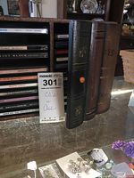 Photo showing a black floral embossed CD storage case alongside stacked music CDs including titles.