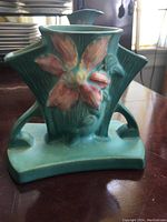 Front view of the clamatis green vase showing the raised pink flower design, geometric handles, and square base.