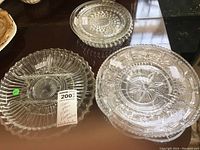 Six clear glass plates and platters of various sizes from 7 to 12 inches with embossed and cut glass patterns on a wooden table.