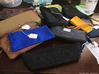 Wide view of various clutch purses and wallets displayed on a table, showing different sizes, styles, and colors including blue, black, brown, yellow, and orange items.