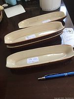 Three vintage ceramic corn dishes arranged side by side on a table with a pen for size reference