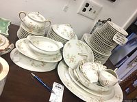 Full set of white Limoges china with pink floral pattern and gold accents including stacked dinner plates, salad plates, cups, covered tureens, and serving bowls.