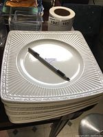 Stack of 8 square cream/off-white Mikasa plates with ribbed and embossed decorative edges and a pen on top for scale.