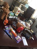 Photo shows assortment of miscellaneous toys on table including wooden carved girl with bear, wooden bear canoe, Pez dispensers, glass dog figurine, snow globe, and boxed items