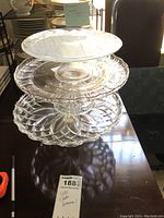 Stacked set of three glass pedestal cake stands on a dark wood table showing decorative clear glass patterns and size differences.