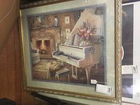 Frontal view of the framed pastel print showing white grand piano, fireplace, floral arrangement, stair railing, ornate gold frame and double matting under glass.
