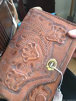 Close-up image of a brown tooled leather purse showing detailed floral and leaf embossing and brass clasp